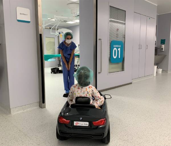 La doctora Jiménez con una paciente pediátrica que conduce un cochecito en la entrada a quirófano.